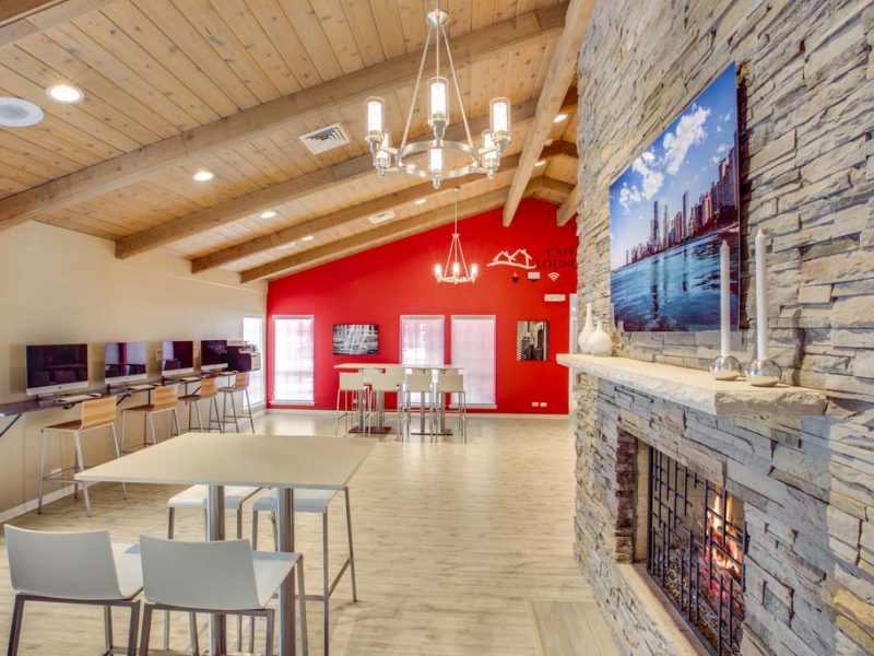 This image exhibits an expansive view of the café lounge and apple computer bar in TGM Willowbrook, featuring elegant chandeliers, wall designs, and a fireplace.